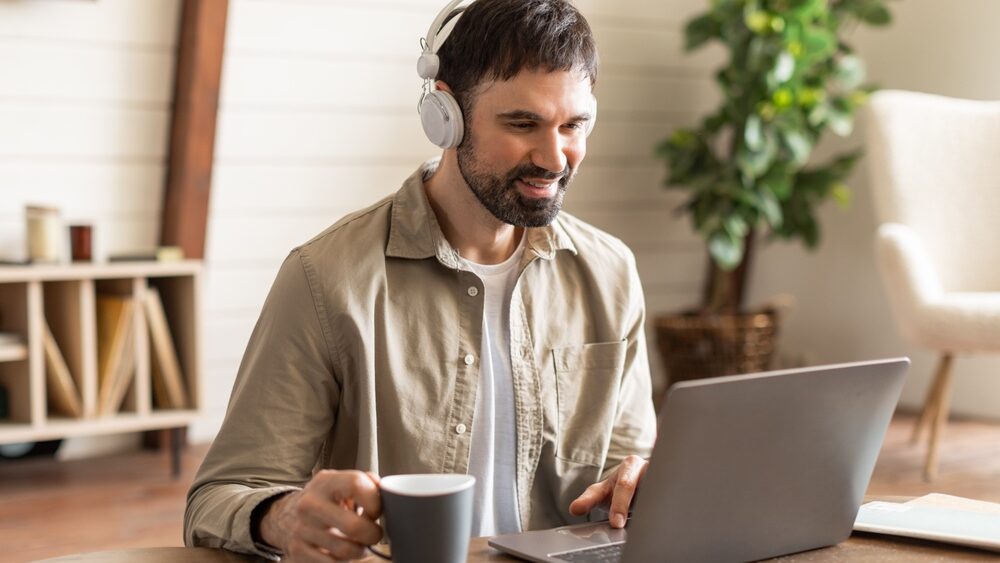 A man enjoying a cup of coffee while watching content on his laptop.